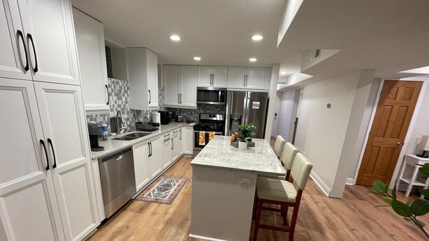 A modern kitchen with white cabinetry, a central island, and a dining area with chairs.