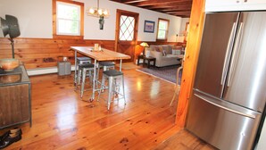 A kitchen with wooden floors, a stainless steel refrigerator, a wooden dining table with stools, and a cozy seating area with a couch and a lamp. - Great Home With Large Yard 300 Yards To Sheep's Pond (2277) (Brewster)