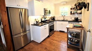 A modern kitchen with stainless steel appliances, white cabinetry, and a wooden floor. - Great Home With Large Yard 300 Yards To Sheep's Pond (2277) (Brewster)