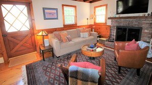 A cozy living room with a fireplace, a sofa, a coffee table, and a TV mounted on the wall. - Great Home With Large Yard 300 Yards To Sheep's Pond (2277) (Brewster)