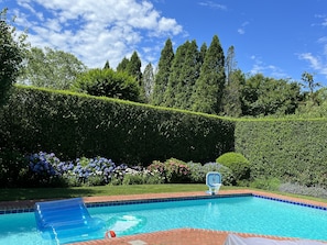 Relax by the serene pool surrounded by lush greenery and a neatly trimmed hedge, perfect for a refreshing dip or a game of basketball.