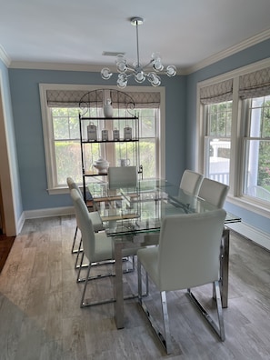 Enjoy meals in this dining area with a glass-top table and six chairs, surrounded by large windows and a stylish shelving unit.
