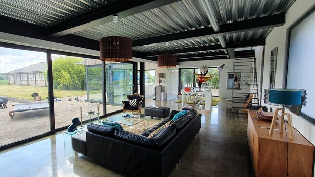 A modern living room with a large glass window, a black leather sofa, and a dining area with a wooden table and chairs. - VILLA COMBINES MODERNITY AND STONES. IDEAL FOR FAMILY OR WORK (LIFFRE)