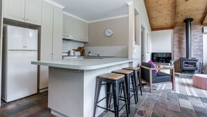 Cocina moderna con armarios blancos, una isla central con taburetes, estufa y chimenea de ladrillo.
