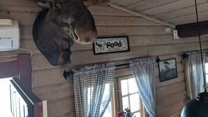 A moose head mounted on a wooden wall, a framed sign, checkered curtains, and a window with a view. - Neset Skydsstasjon (Flesberg)