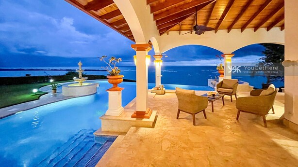 Een luxe buitenzwembad met uitzicht op zee, met een pergola, zitplaatsen en een fontein.