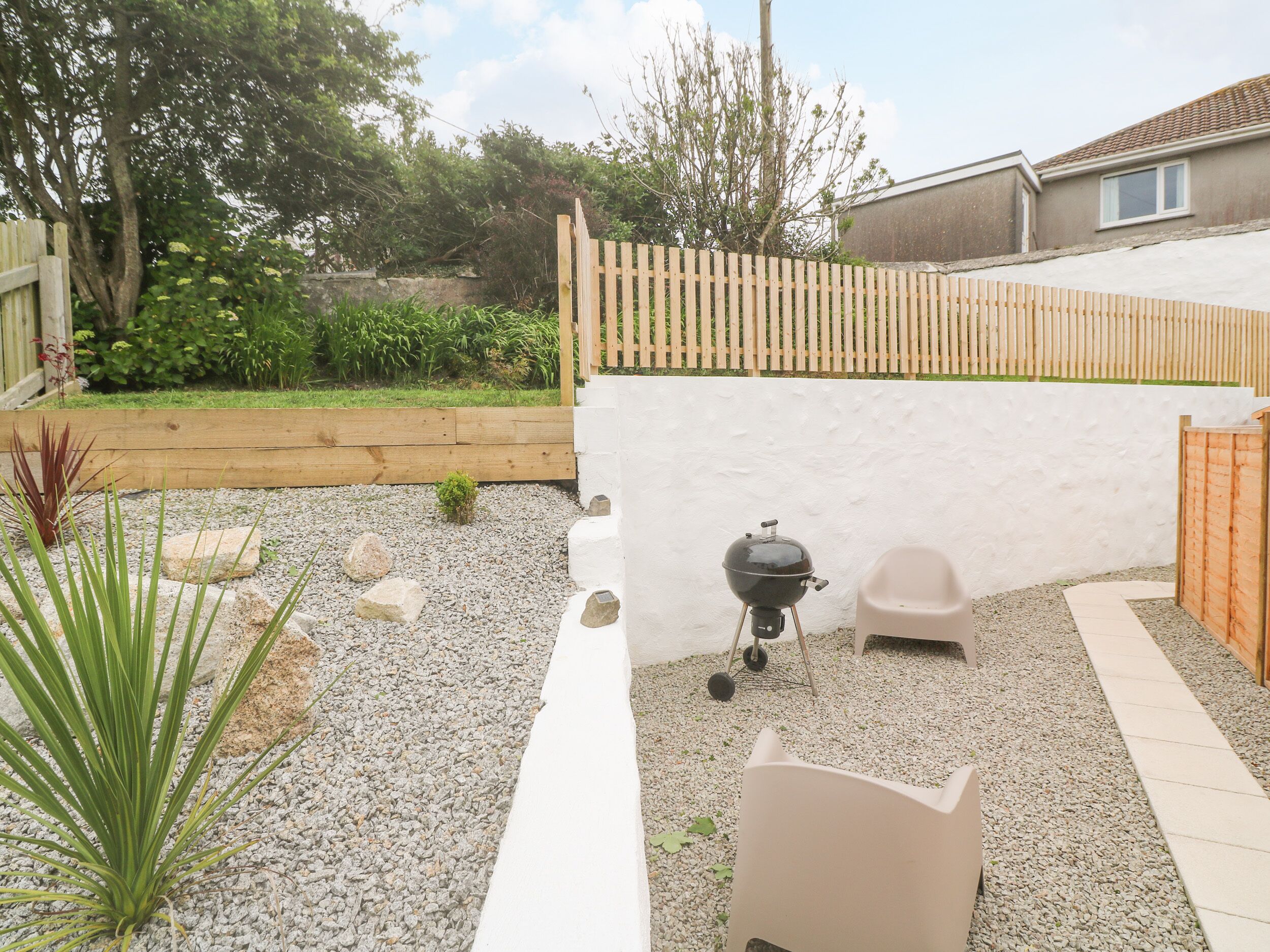Un giardino sul retro con un barbecue, una sedia bianca e una piccola pianta.