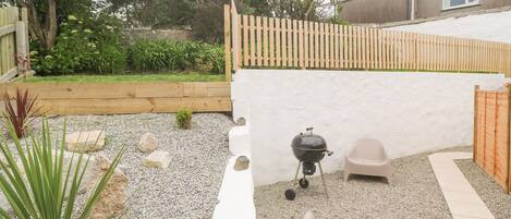 Un giardino sul retro con un barbecue, una sedia bianca e una piccola pianta.