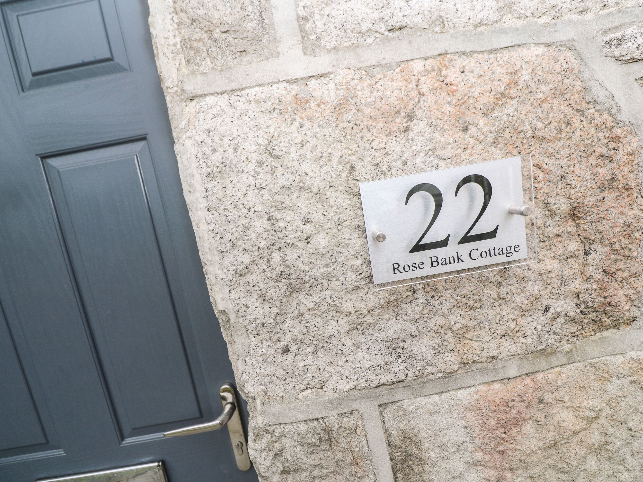 A house number plaque on a stone wall, indicating '22 Rose Bank Cottage.'