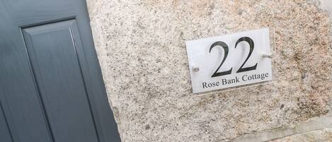 Una placa con el número de casa en una pared de piedra, que indica '22 Rose Bank Cottage'.