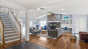 A spacious living area with a stone fireplace, a staircase, and a bookshelf. - Lake Therapy On Keuka | Lakefront | FLX | Hot Tub (Branchport)