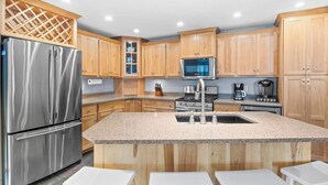 A modern kitchen with wooden cabinets, stainless steel appliances, granite countertops, and a central island with bar stools. - Lake Therapy On Keuka | Lakefront | FLX | Hot Tub (Branchport)