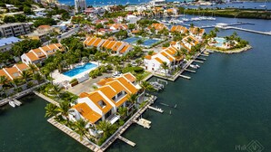 Vista aérea de un complejo turístico costero con varias edificaciones, un puerto deportivo y una piscina.