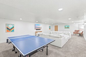 A room with a ping pong table, a white sofa, and a small table with a lamp.