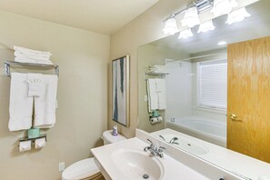 A bathroom with a sink, mirror, and toilet. There are towels on a rack and a painting on the wall.