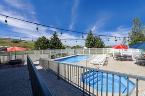 A swimming pool with a white fence, lounge chairs, and umbrellas.