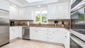 Una cocina moderna con armarios blancos, encimeras de granito, electrodomésticos de acero inoxidable y un tragaluz.