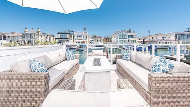 Un patio frente al agua con mobiliario de mimbre, una mesa de hormigón y vistas a casas y barcos.