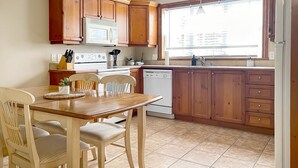 Een keuken met houten kastjes, een magnetron, een fornuis en een vaatwasser. Er is een eettafel met stoelen en een raam dat natuurlijk licht biedt.