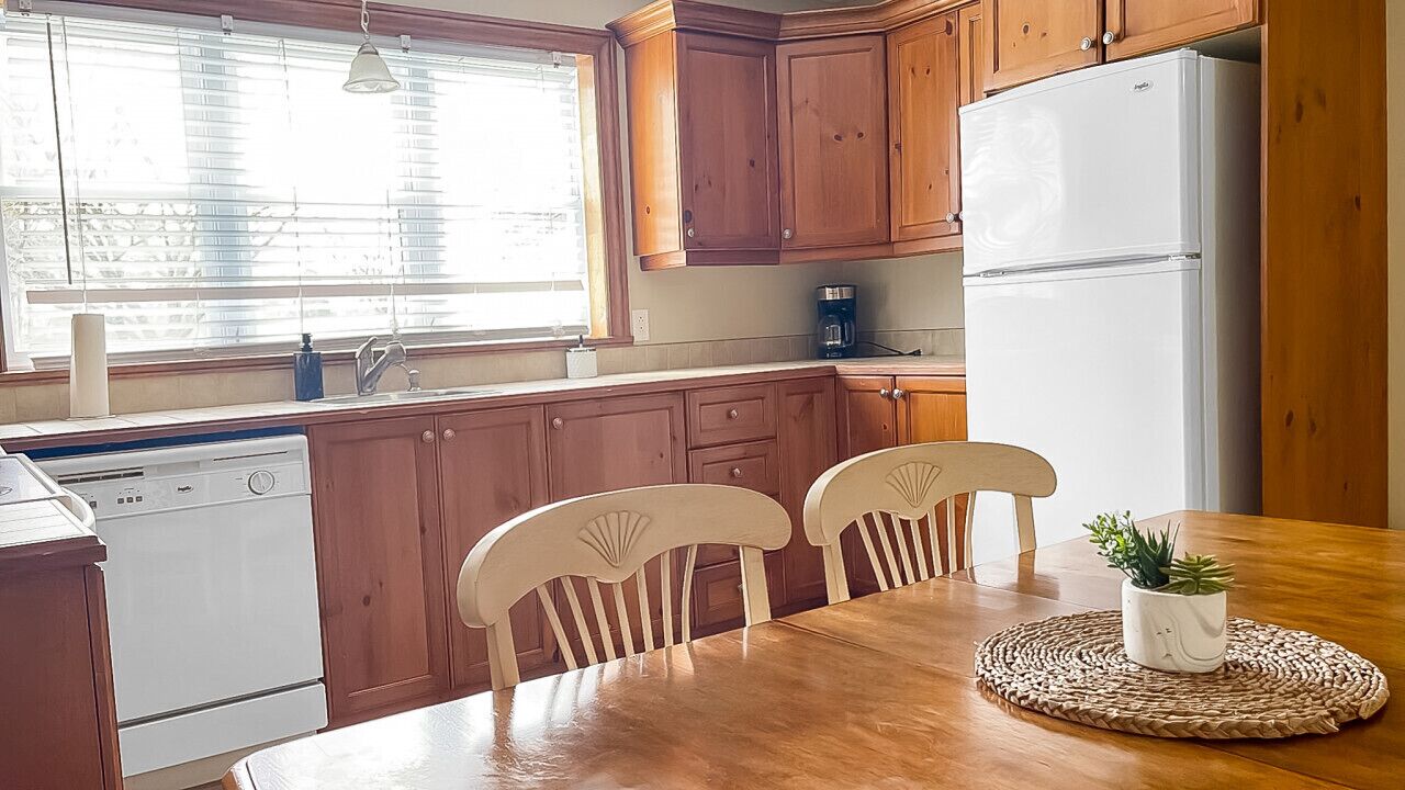 A kitchen with wooden cabinets, a white refrigerator, a coffee maker, and a dining table with chairs.