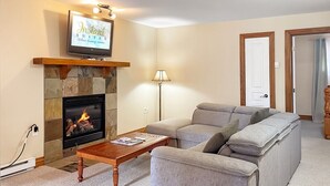 Een woonkamer met een stenen openhaard, een televisie erboven, een bank, een lamp en een deur.