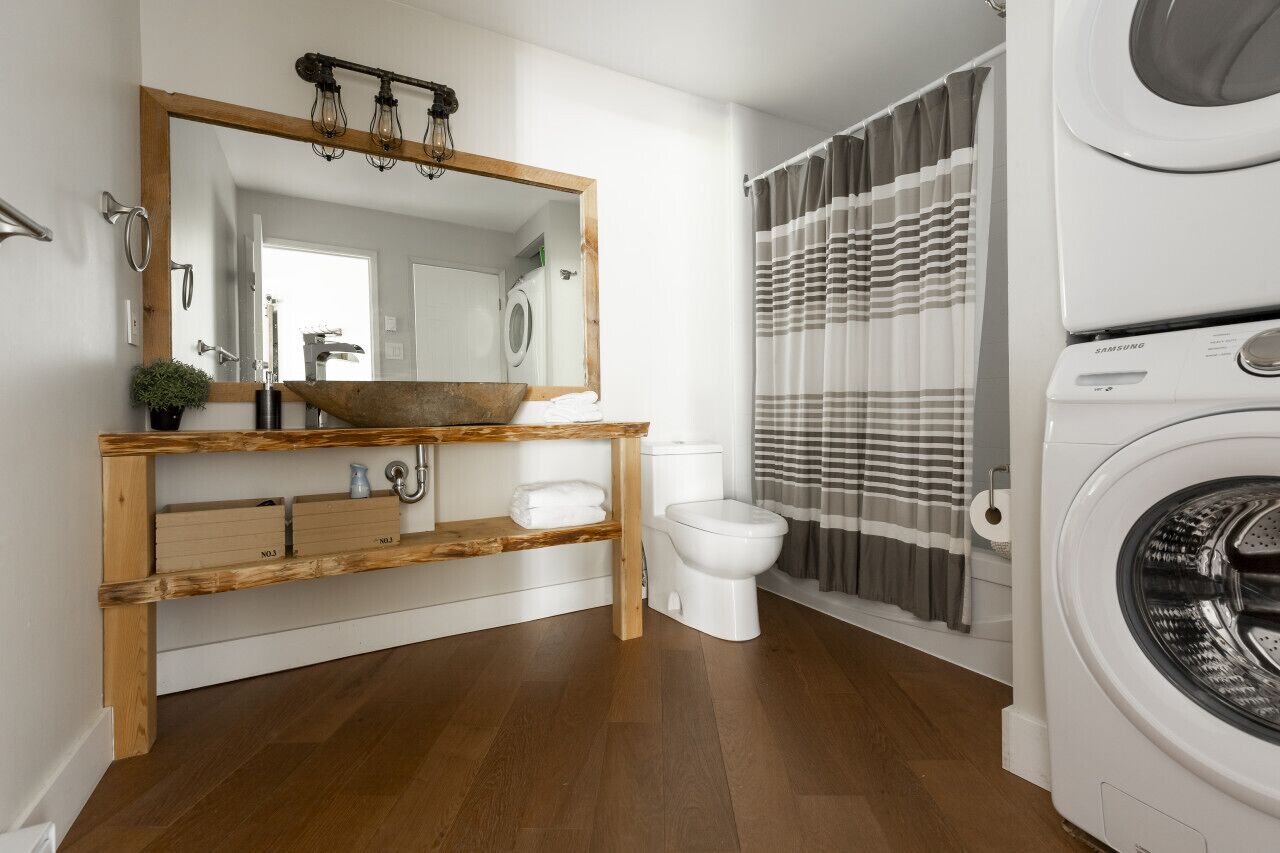 Une salle de bain moderne avec un meuble-lavabo en bois, un grand miroir, un lavabo, des toilettes et un lave-linge.