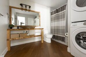 Ein modernes Badezimmer mit einem Holzbadezimmerunterschrank, einem großen Spiegel, einem Waschbecken, einer Toilette und einer Waschmaschine.
