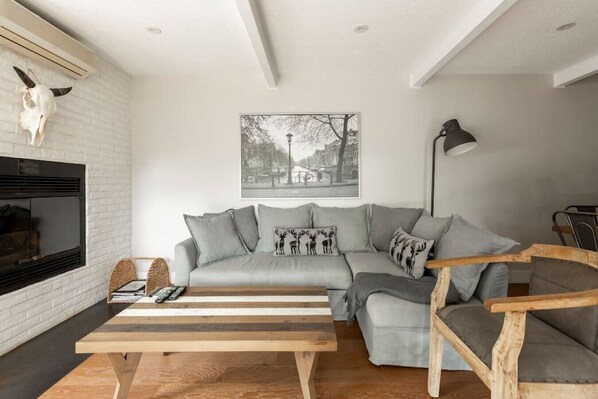 Ein modernes Wohnzimmer mit einem grauen Ecksofa, einem Holztisch, einem Kamin und einem Wandbild.