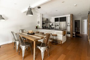 Eine moderne Küche mit einer zentralen Kochinsel, Edelstahlgeräten und einem Essbereich mit Holztisch und Metallstühlen.