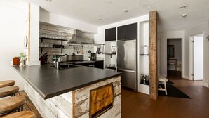 Une cuisine moderne dotée d’un îlot central, d’appareils électroménagers en acier inoxydable et d’un mur d’accent en briques au style rustique.