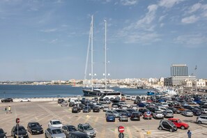 A parking lot with cars and a sailboat in the background. - Casetta del Pescatore (Gallipoli)