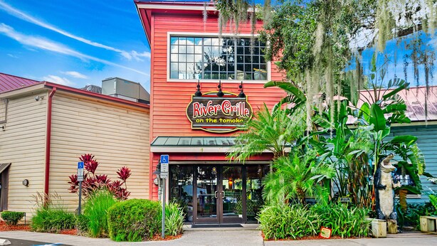 Un restaurant appelé River Grille, reconnaissable à sa façade rouge, à ses grandes fenêtres et aux plantes tropicales qui l’ornent.