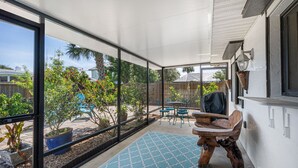 Une terrasse couverte donnant sur un jardin, avec une table en bois, des chaises et des plantes en pot.