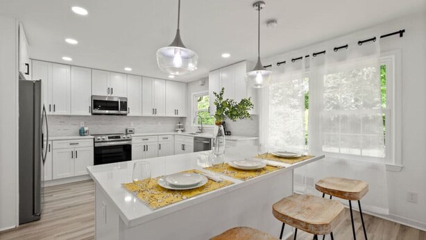 Una cocina moderna con armarios blancos, una isla central, taburetes de bar e iluminación colgante.