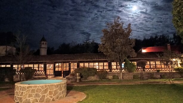 A stone pool, a building with a tiled roof, and a tree in a garden at night. - Hacienda Santiago Texmelucan (Oriental)