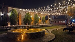 An outdoor area with stone walls, a circular fountain, string lights, and tables set up for dining. - Hacienda Santiago Texmelucan (Oriental)
