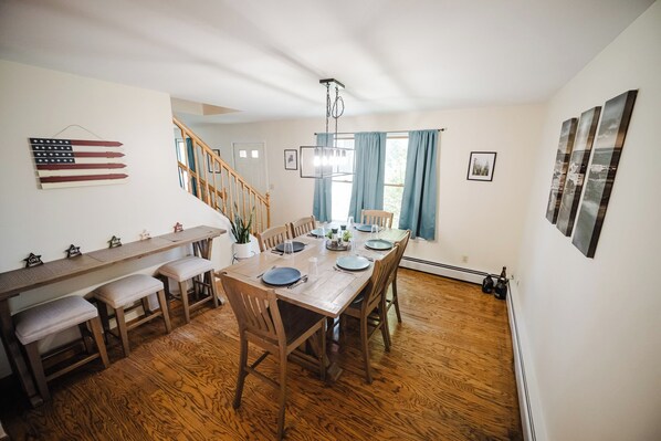 Un comedor con una mesa de madera dispuesta para cuatro personas, bancos a lo largo de una pared y una escalera al fondo.