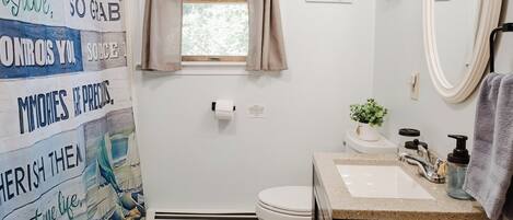 A bathroom with a shower curtain featuring motivational quotes, a window with curtains, a sink with a mirror, and a towel rack.