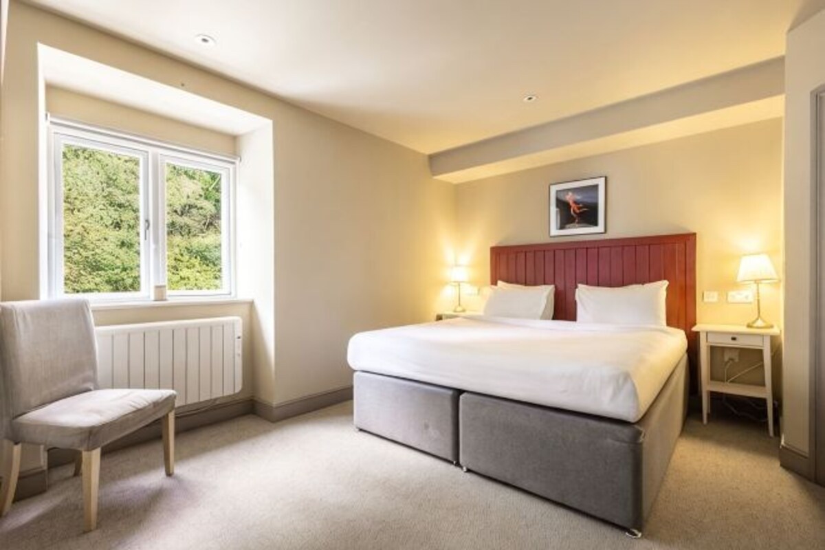 Een hotelkamer met een bed, twee nachtkastjes, een stoel, een raam met uitzicht en een radiator.