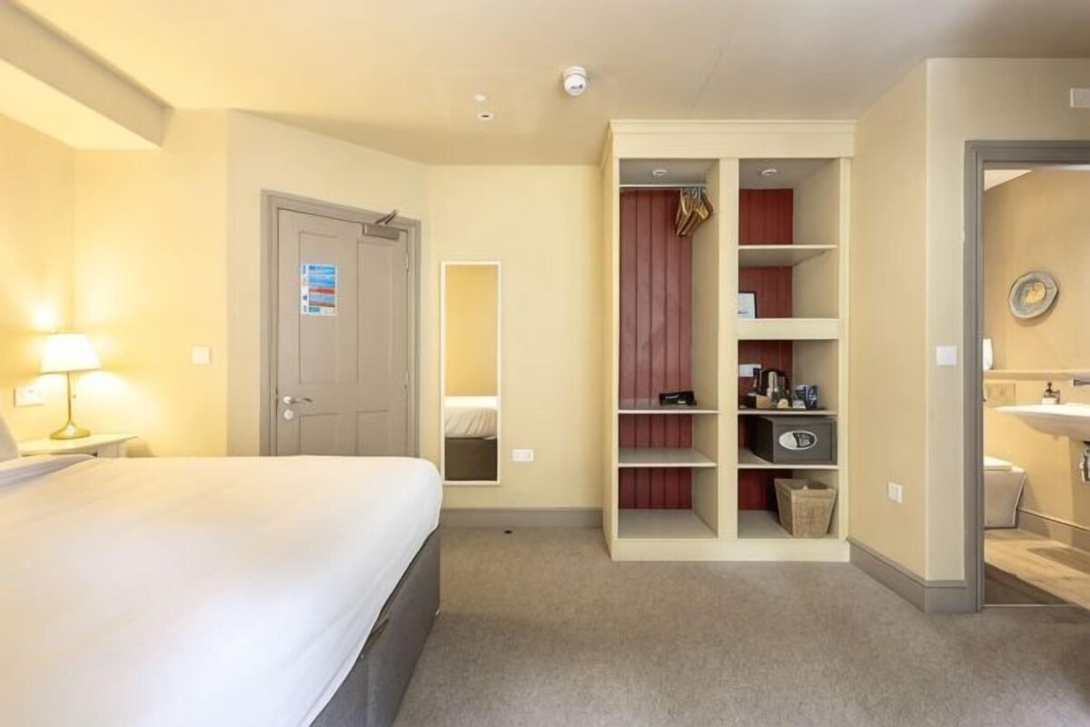 A hotel room with a bed, a wardrobe, a bathroom, and a desk with a lamp.