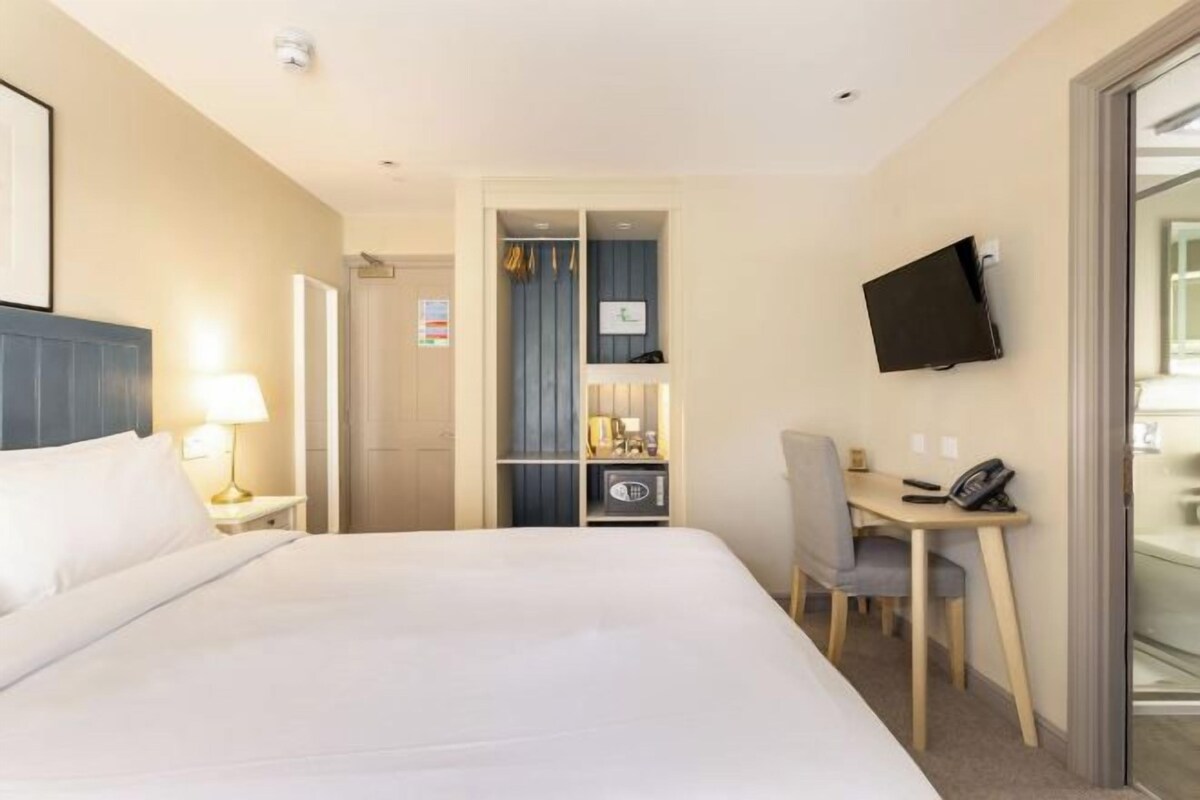 A hotel room with a bed, a desk, a chair, a television, and a wardrobe.