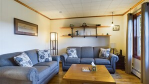 A living room with two grey sofas, a wooden coffee table, and a floor lamp. Shelves with decorative items are above the sofas. - 20 Minutes to Munising, Quiet Country Setting (Eben Junction)