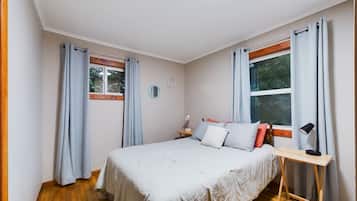Un dormitorio con cama, mesita de noche, lámpara, ventana y cortinas.
