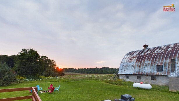 A rustic barn with a metal roof, a wooden deck, and a barbecue setup in a grassy field. - 20 Minutes to Munising, Quiet Country Setting (Eben Junction)