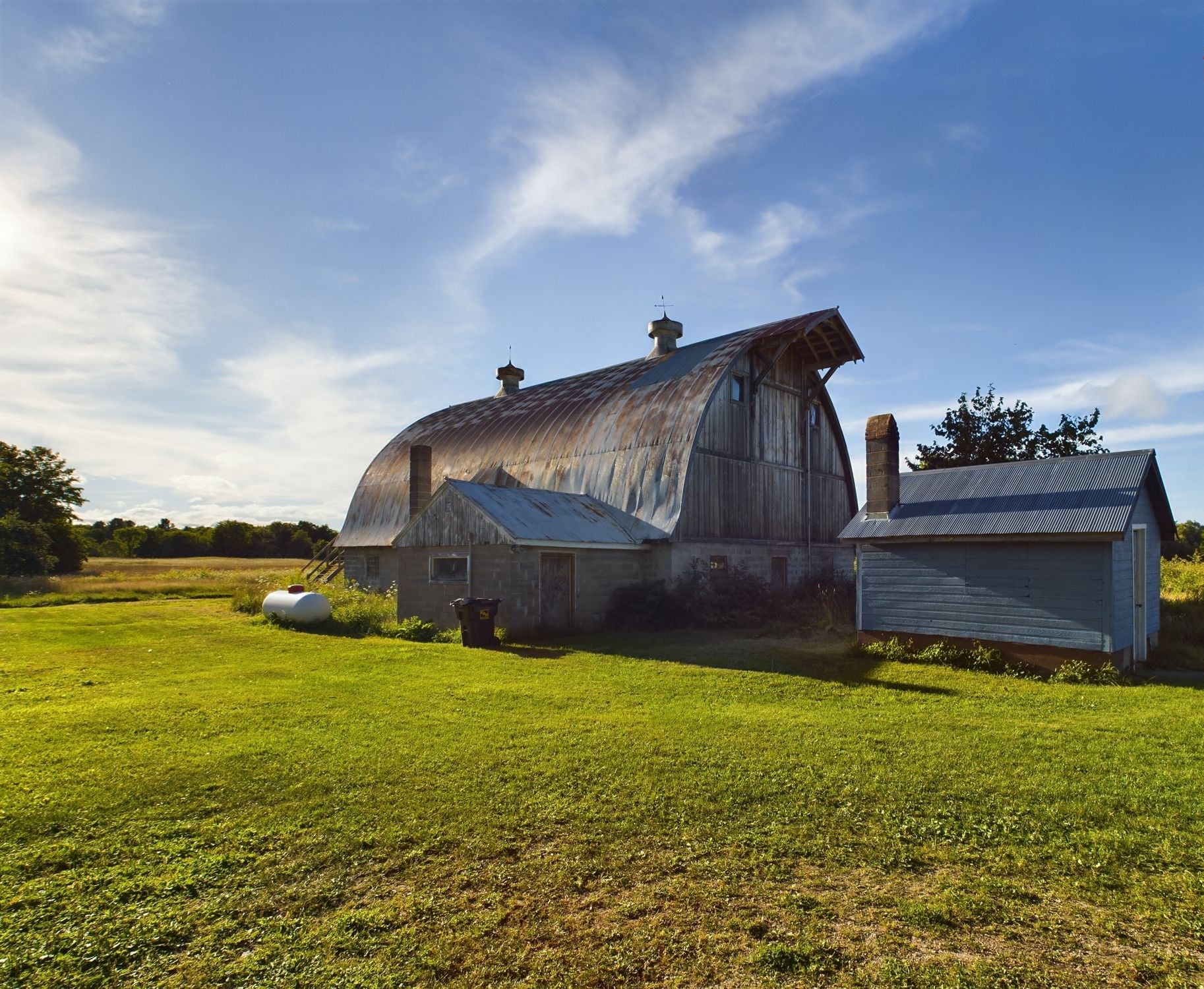 A rustic barn with a large, curved roof and a smaller attached structure.