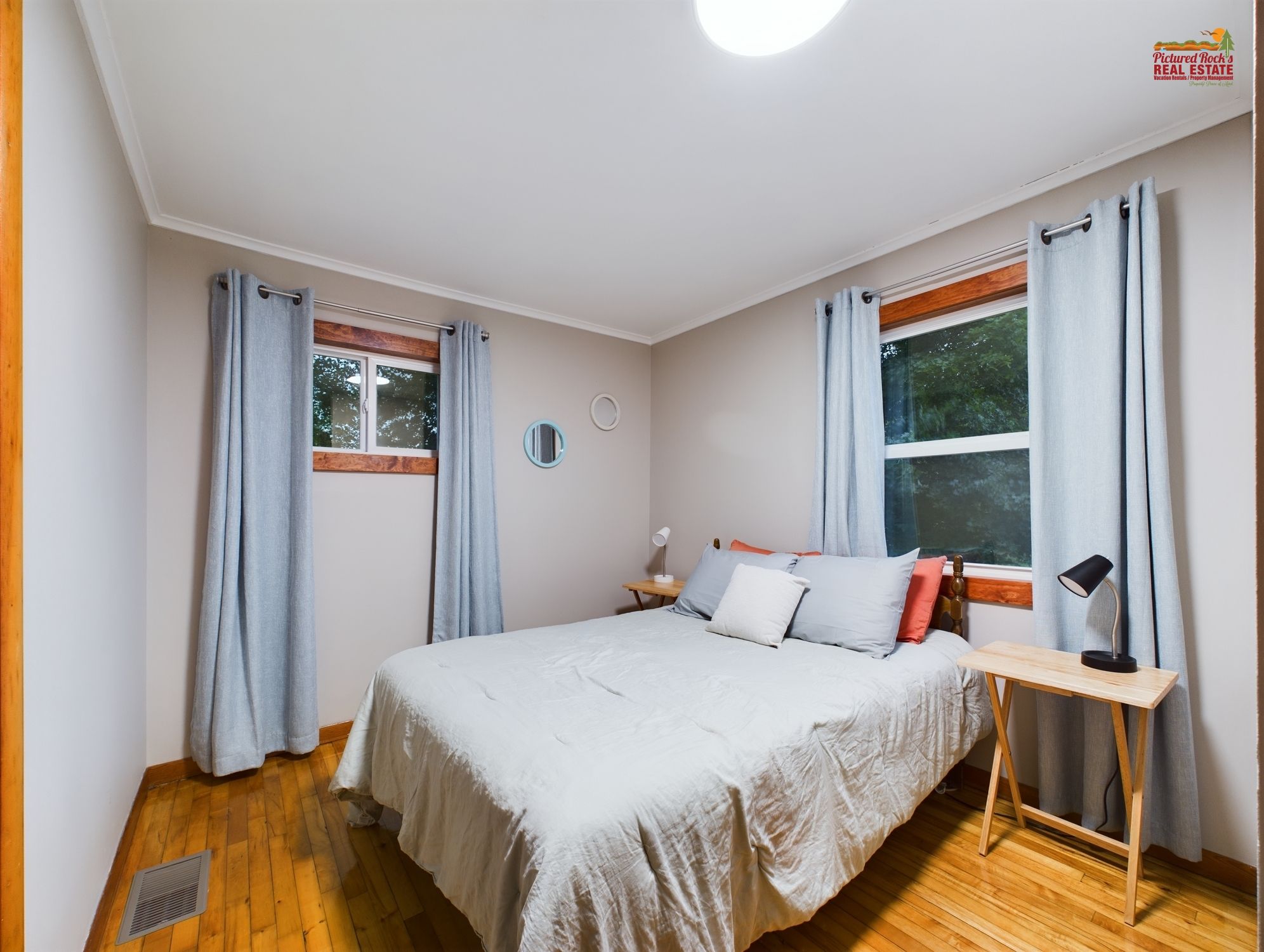 A bedroom with a bed, a bedside table, a lamp, a window, and curtains.