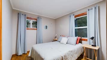 A bedroom with a bed, a bedside table, a lamp, a window, and curtains.