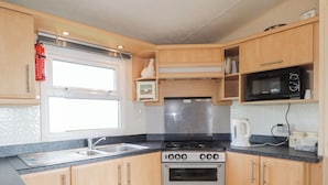 A compact kitchen with wooden cabinets, a gas stove, an oven, a microwave, and a sink.