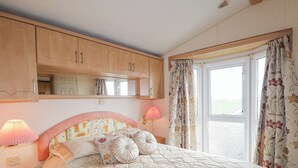 A bedroom with a bed, two bedside lamps, a mirror, and a window with curtains.