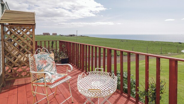A covered outdoor area with a red railing, a white metal table, and two patterned chairs.